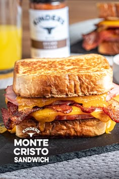 a grilled cheese and bacon sandwich on a black plate with orange juice in the background