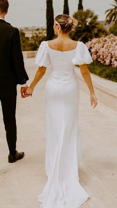 a bride and groom holding hands while walking down the sidewalk in front of palm trees