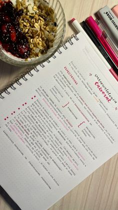 a bowl of granola next to a recipe book on a table with pens and markers