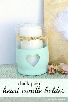 a candle holder with two white candles in it and a heart painted on the front