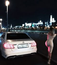 a woman in tight dress leaning against a car on the side of the road at night