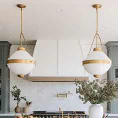 two lights hanging from the ceiling above a kitchen island with marble counter tops and gold accents