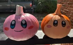 two pumpkins with faces painted on them sitting on a wooden bench next to each other