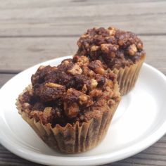 two muffins on a white plate sitting on top of a wooden table next to each other