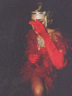 a woman in a red dress and feathered gloves is holding her hands up to her face