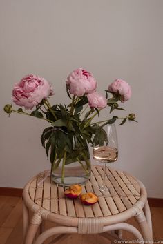 some pink flowers are in a vase on a small table with a glass of wine