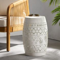 a white vase sitting on top of a table next to a chair and potted plant