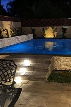 an outdoor pool lit up at night with lights on the side and water running through it