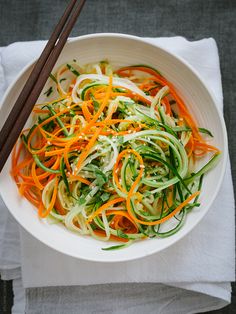 a white bowl filled with veggies and chopsticks on top of a table