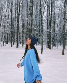 a woman standing in the snow with her arms out and looking up to the sky