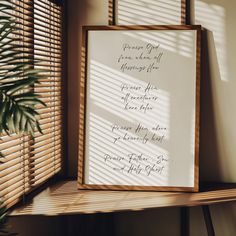 a framed poem on a shelf next to a window with blinds and a potted plant