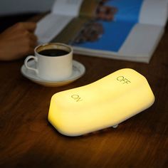 a yellow light sitting on top of a wooden table next to a cup of coffee