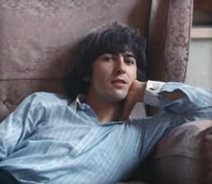 a young man laying on top of a couch next to a wall with a remote control in his hand