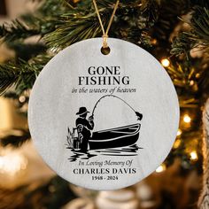 a christmas ornament hanging from a tree with a fishing scene on it and the words gone fishing in the waters of heaven