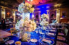 a tall vase filled with white flowers sitting on top of a blue table covered in plates