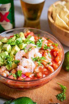 a glass bowl filled with shrimp and guacamole next to a wooden cutting board