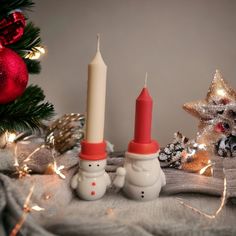 two snowmen are next to a lit candle on a blanket with christmas decorations in the background