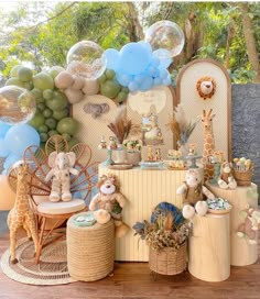 a table topped with lots of balloons and stuffed animals next to a wall covered in giraffes