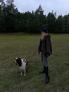 a woman walking her dog on a leash in a field with trees in the background