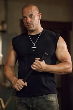 a bald man with a cross on his chest holding a knife in one hand and looking at the camera