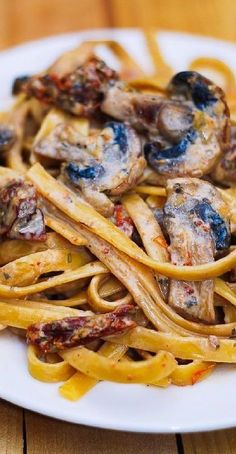 a white plate topped with pasta covered in mushrooms and sauce on top of a wooden table