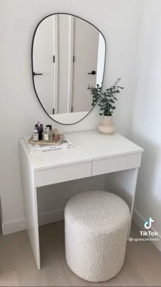 a white vanity table with a mirror and stool in front of it, next to a potted plant