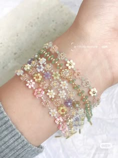 a woman's arm with several bracelets and flowers on it, all in pastel colors