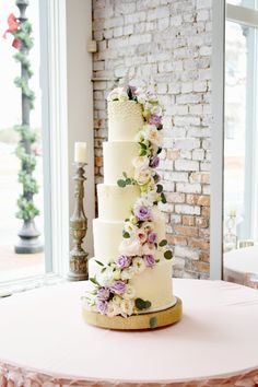 a wedding cake with flowers on it sitting on a table in front of a brick wall