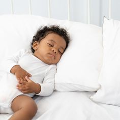 a small child sleeping on top of a bed with white sheets and pillowcases