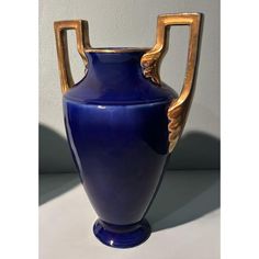 a large blue vase with gold handles on a white counter top next to a wall