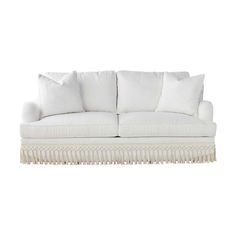 a white couch with pillows on it and fringe trim around the armrests, sitting in front of a white background