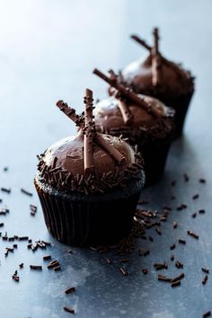 three cupcakes with chocolate frosting and sprinkles on a table