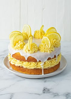 a cake with lemons and icing sitting on a white plate next to a marble counter