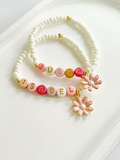 two bracelets with name beads and flower charms on them sitting on a tray next to each other