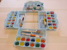 four trays filled with paint and brushes on top of a table