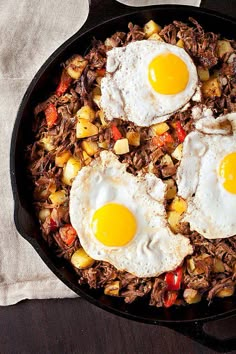 two fried eggs in a skillet with sausage and potatoes