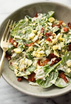 a salad with bacon, lettuce and eggs in a bowl next to a fork