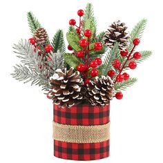 a red and black plaid vase filled with pine cones, berries and evergreen branches on a white background