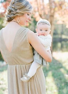 a woman holding a baby in her arms while wearing a dress and pearls on it's head