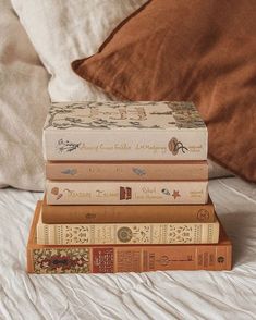 a stack of books sitting on top of a bed next to a brown throw pillow