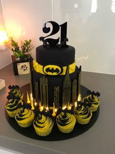 a batman themed birthday cake with cupcakes and candles