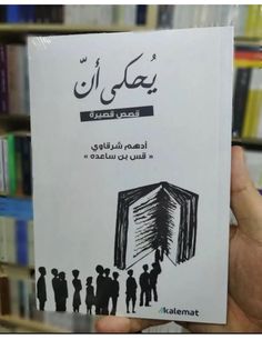 a person holding up a book in front of bookshelves with arabic writing on it