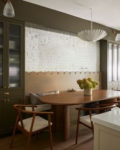 a dining room table and chairs in front of a white brick wall with wood trim