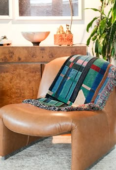 a brown leather chair with a patchwork pillow on it's back in front of a wooden dresser