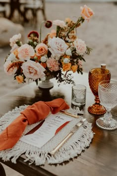 the table is set with an orange napkin, glassware and flowers in vases