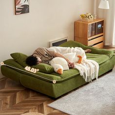 a man laying on top of a green couch in a living room next to a window