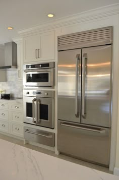 a kitchen with stainless steel appliances and marble counter tops, along with white cabinetry