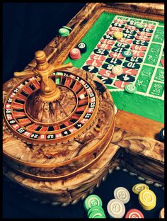 a wooden table topped with a rouleet and lots of casino chips