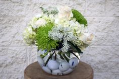 a vase filled with white flowers and golf balls on top of a wooden table next to a brick wall