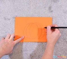 someone is drawing a pumpkin on an orange piece of paper